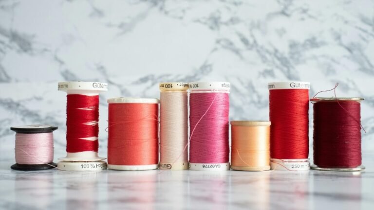 Carretéis de linhas de costura de diferentes cores e materiais organizados sobre uma superfície clara.