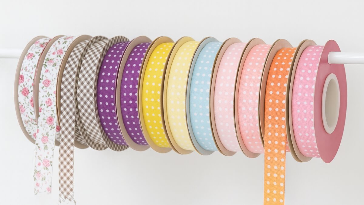 Viés de tecido colorido pendurados lado a lado em rolinhos na frente de uma parede clara